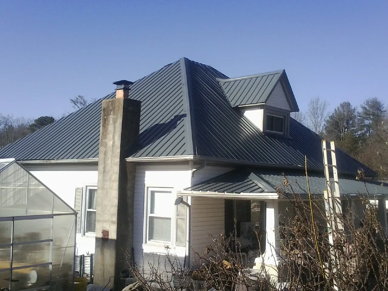 Dark blue standing seam metal roof on a white farmhouse with dormer — Slate & Tile Roof Repair by Roofing Brothers in Treadwell