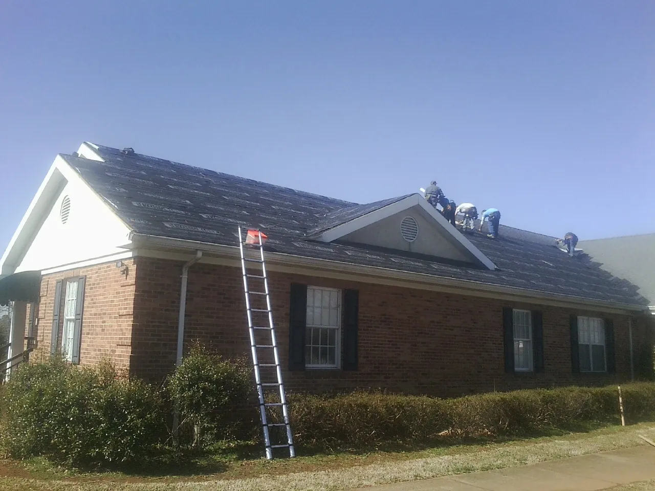 Crew tearing shingles off a brick ranch roof with a ladder set — Metal Roof Repair work by our crew in Treadwell