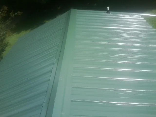 New green metal panels meeting at the ridge of a roof — Flat Roof Repair work by our crew in Treadwell