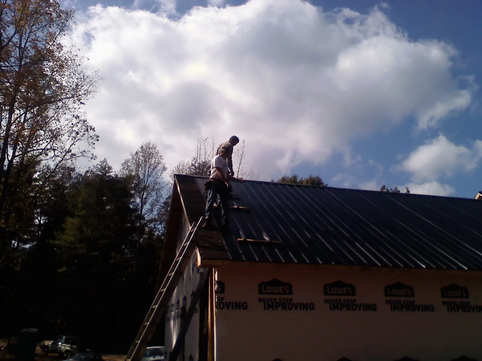Roofer fastening dark metal panels high against a cloudy sky, from a Roof Inspection job in Treadwell