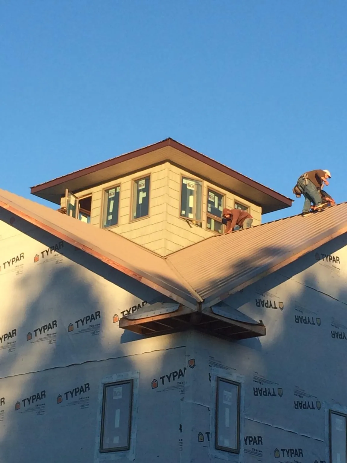 Roofers working around a rooftop cupola on a new metal roof at sunset — Roof Waterproofing in Treadwell by Roofing Brothers